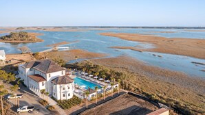 Une propriété située sur la côte, dotée d’une piscine, offrant une vue sur la plage et comprenant un grand bâtiment blanc.