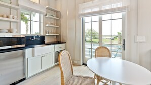 Une cuisine moderne avec des meubles blancs, un four à micro-ondes encastré et un coin repas agrémenté de chaises en osier et d’une table blanche.