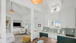 A modern kitchen with white cabinets, a wooden dining table, and a large window. - “Eagles Nest” (3035 Southerly Way) 2 person creekside bungalow at Kiawah River ~ (Johns Island)