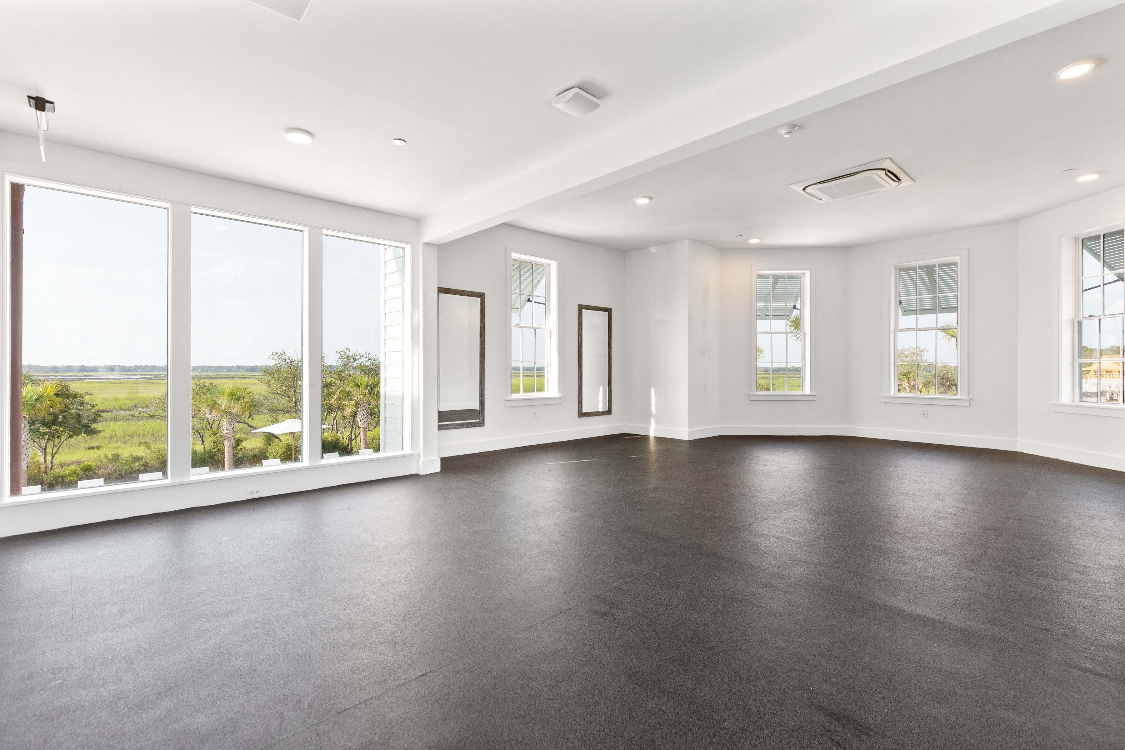A spacious room with large windows, a dark floor, and white walls.