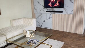 A modern living room with a marble wall, a flat-screen TV, a white sofa, and a glass coffee table.