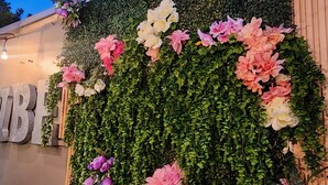 A wall decorated with various flowers and greenery, with a wooden fence and a sign with letters visible.