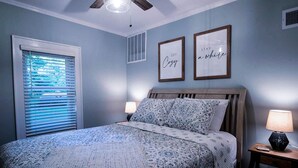 Un dormitorio con cama, dos lámparas de noche, un ventilador de techo y dos citas enmarcadas en la pared.