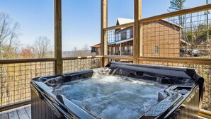 Un jacuzzi en una terraza de madera con vistas a una cabaña y árboles.