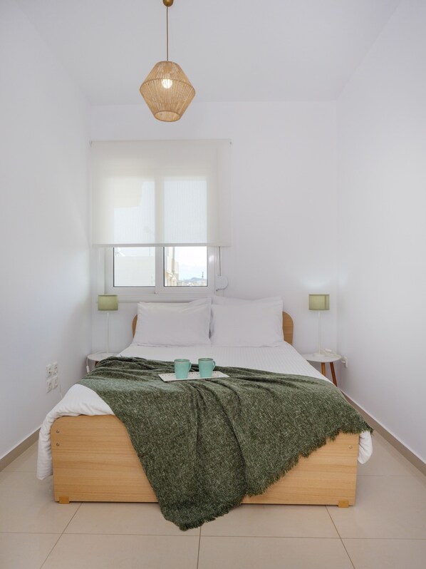 A minimalist bedroom with a wooden bed, a green throw blanket, and two bedside lamps.