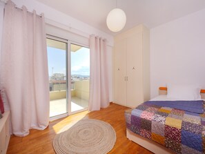 A bedroom with a large window, a bed with a colorful quilt, a wardrobe, and a round rug.