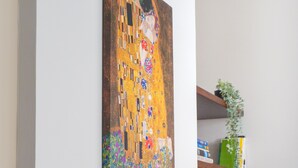 Un cuadro que muestra a una pareja abrazándose en una pared, un estante de madera con plantas, y un televisor al fondo.