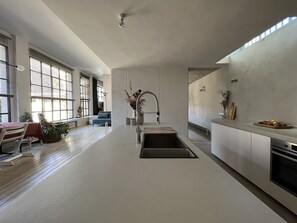 A modern kitchen with a central island, a dining area with a table and chairs, and large windows allowing natural light.