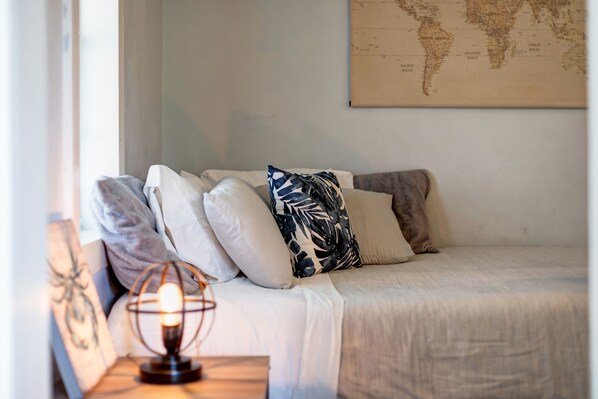 A neatly arranged bed with multiple pillows, a world map on the wall, and a table with a lamp and a decorative item.
