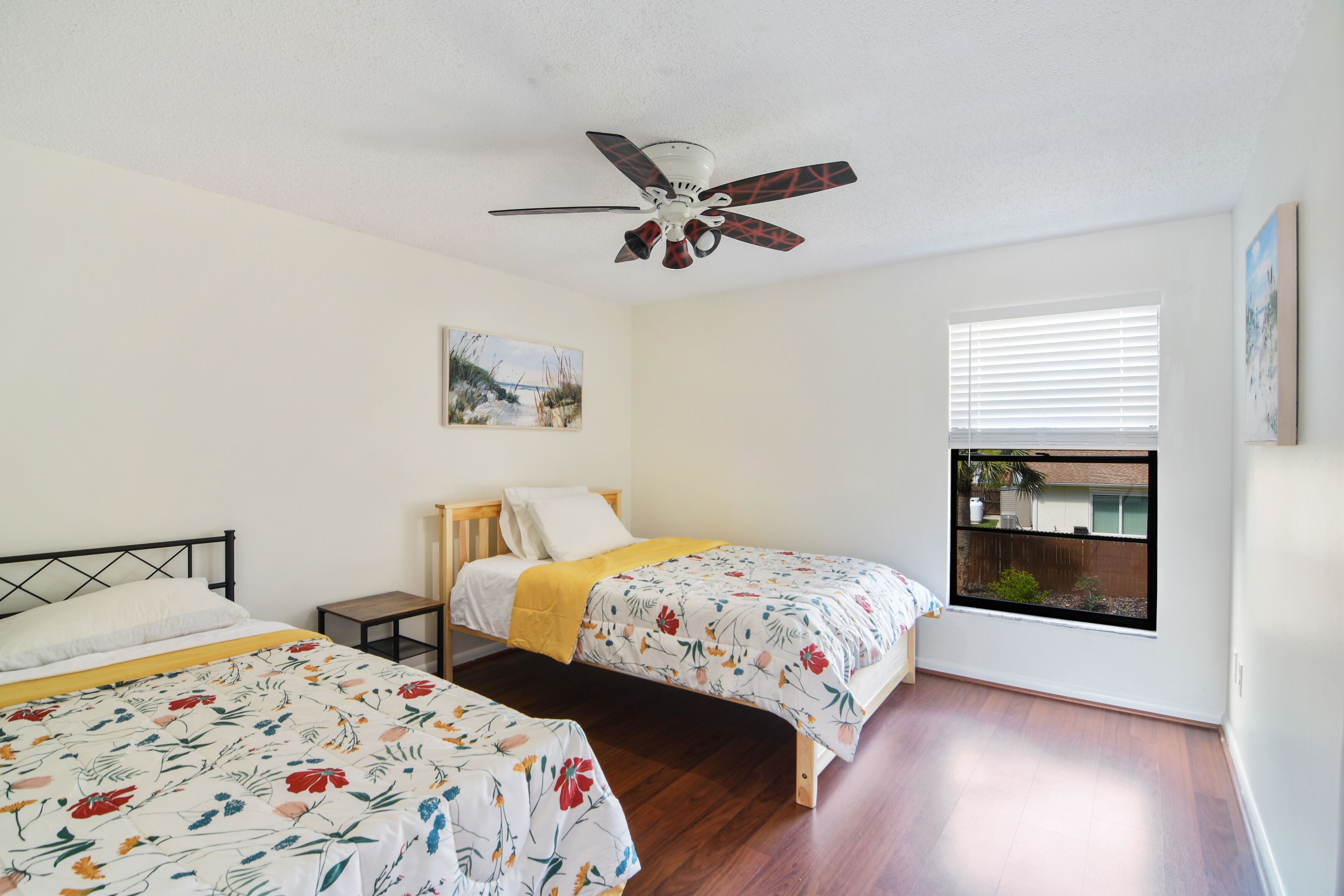 A bedroom with two single beds, a ceiling fan, a window with a view, and a small table.