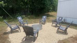 A gravel patio with six lounge chairs and a round table, surrounded by trees and a white building. - FS Rental #2 Annapolis, MO Black River (Annapolis)