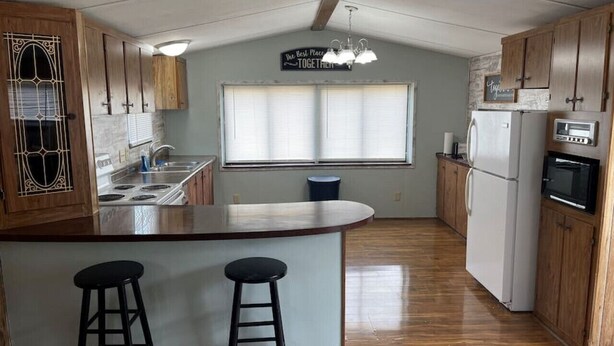 A kitchen with wooden cabinets, a central island with stools, a refrigerator, and a microwave. - FS Rental #2 Annapolis, MO Black River (Annapolis)
