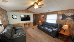 A living room with two leather sofas, a ceiling fan, a flat-screen TV, and wooden paneling on the walls. - FS Rental #2 Annapolis, MO Black River (Annapolis)
