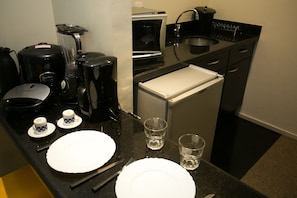 Cocina compacta equipada con refrigerador, microondas, cafetera y pileta.
