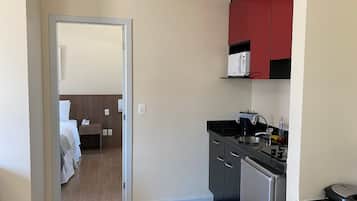 Una habitación de hotel compacta con kitchenette, una cama con ropa blanca y suelo de madera.