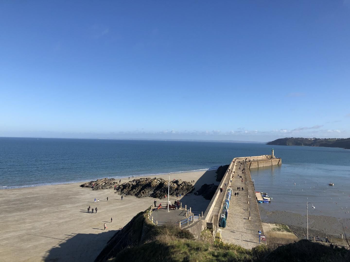 Eine Küstenpromenade mit Betonweg, Strand und Felsformationen.