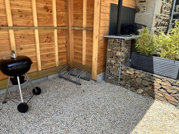 A wooden outdoor grill area with a stone wall and a metal rack.