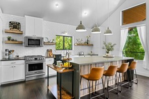 Una cocina moderna con armarios blancos, una isla central con taburetes y luminarias colgantes.