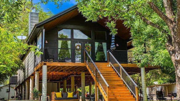 Ein zweistöckiges Haus mit einer Holzterrasse, einer Treppe und einem überdachten Sitzbereich im Freien.