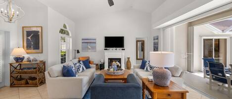 A spacious living room with a fireplace, a ceiling fan, and a large TV.