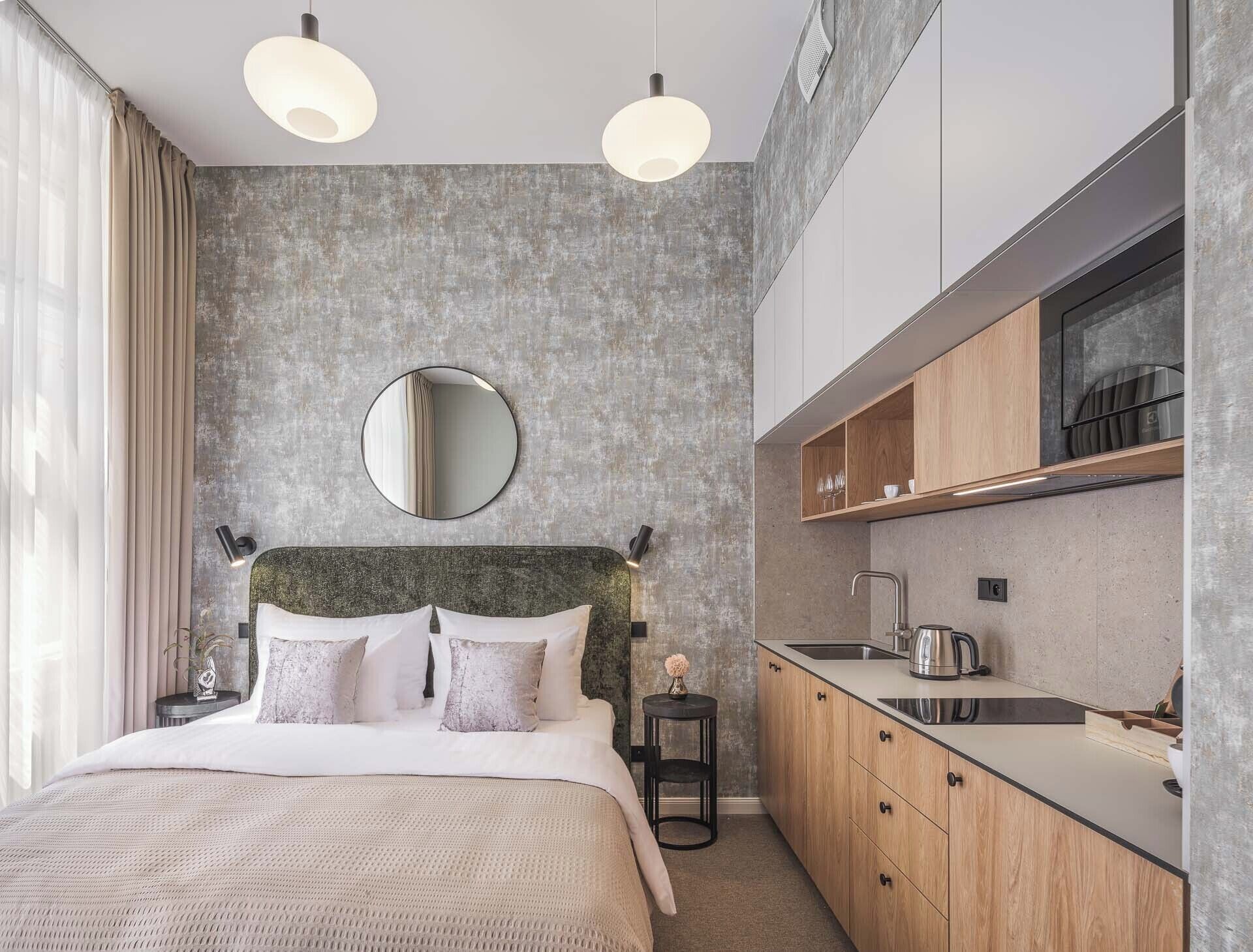 A modern bedroom with a large bed, a round mirror, and a built-in kitchen with wooden cabinets and a sink.