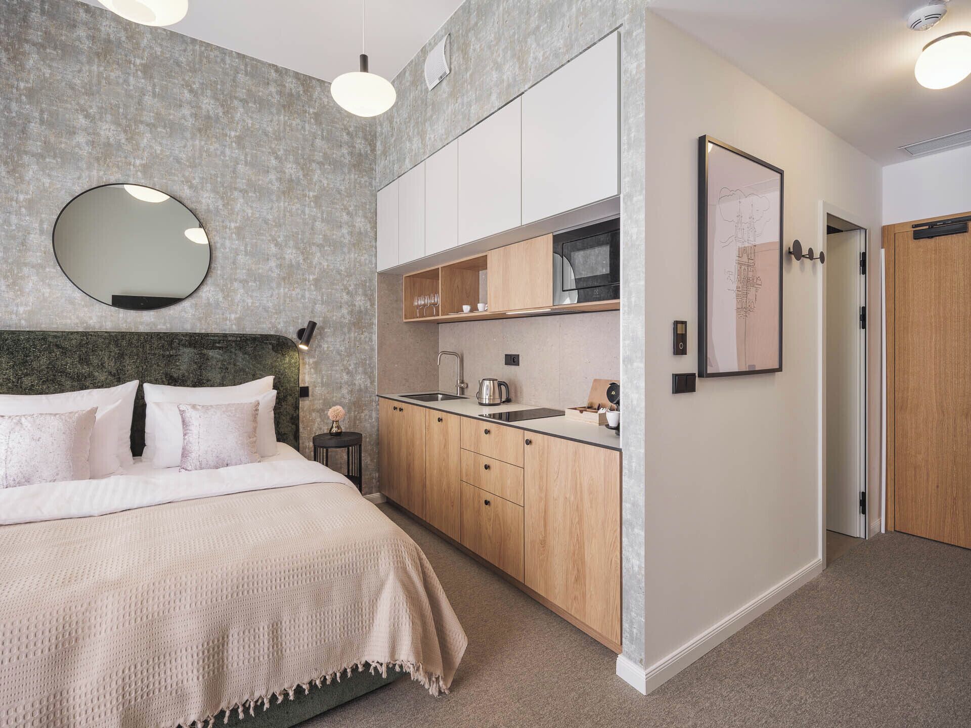 A modern bedroom with a bed, bedside table, and a built-in kitchen area with cabinets and a microwave.