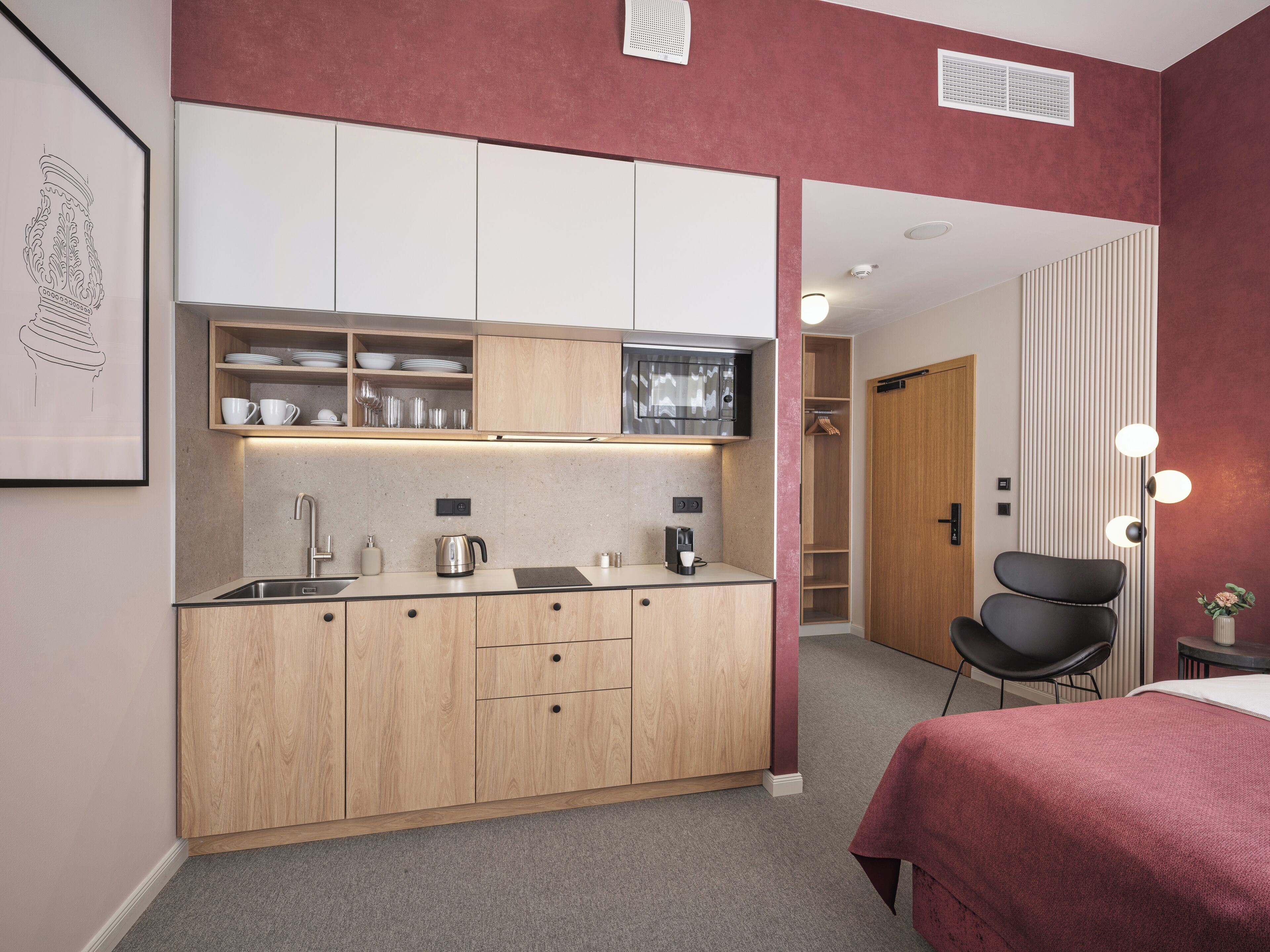 Cocina compacta con muebles de madera, un lavamanos y una encimera. Cuenta con una pequeña zona de estar con una silla y una mesa.