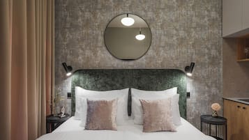 Quarto com parede texturizada, espelho redondo, cama com almofadas brancas e rosa, e abajures laterais.