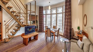 Un salon moderne avec un escalier en bois, un coin repas et une grande fenêtre agrémentée de rideaux à motifs.