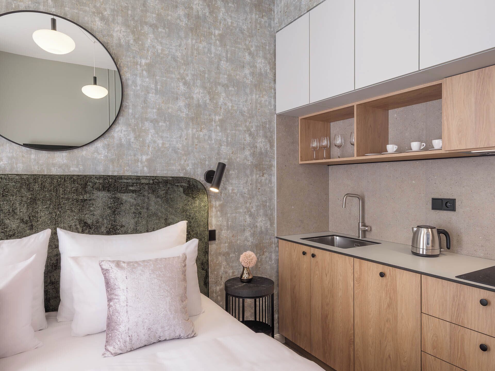 A modern bedroom with a large bed, a round mirror, and a small bedside table with a vase.