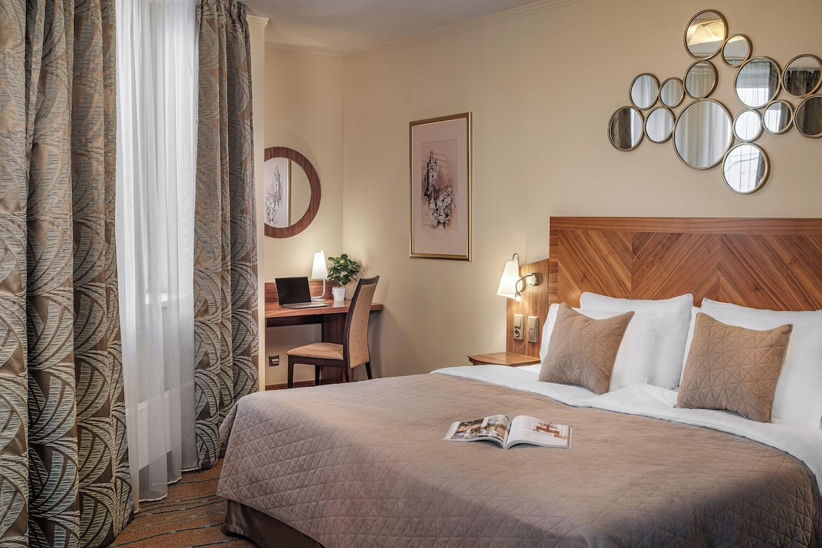 A hotel room with a bed, a desk with a laptop, a chair, a lamp, and a wall with mirrors.