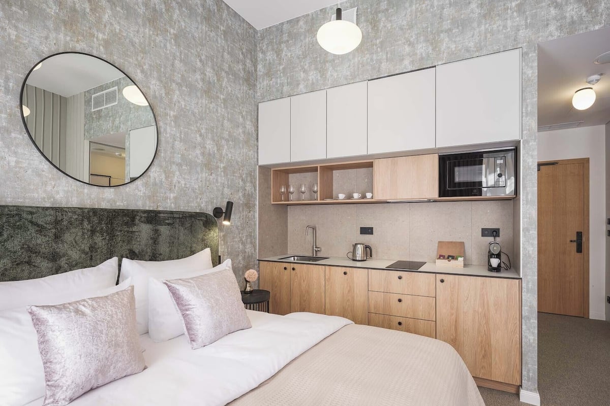 A bedroom with a large bed, a round mirror, and a kitchenette with a microwave and coffee maker.