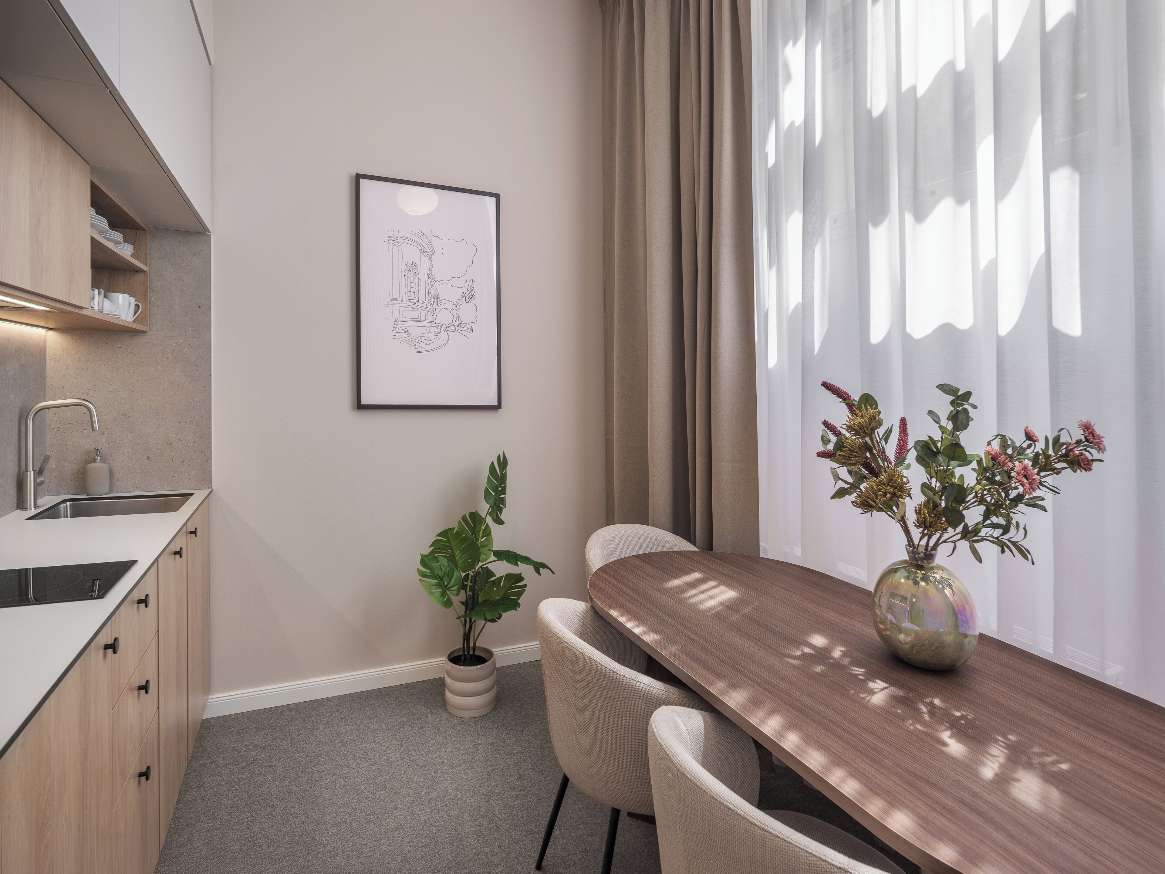 A modern kitchen with a built-in sink, a dining area with a wooden table and chairs, a potted plant, and a framed artwork on the wall.