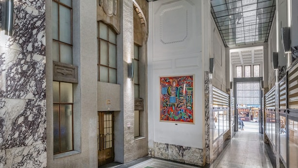 Un couloir aux murs de marbre, orné d’une grande fresque murale et surmonté d’un plafond de verre.