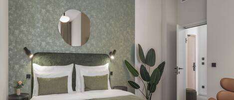 A modern hotel room with a large bed, a round mirror, a potted plant, and a seating area.