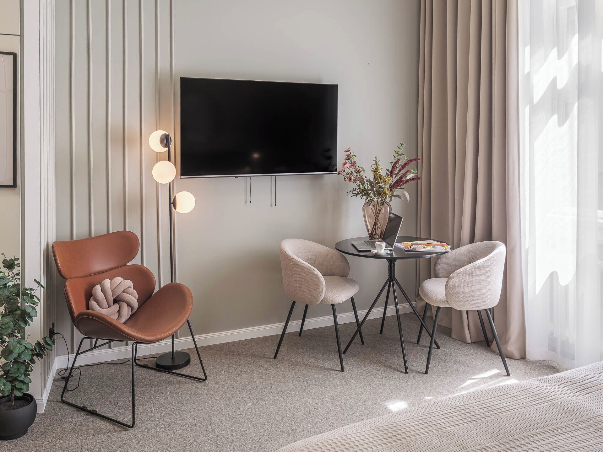 En moderne stue med et fladskærms TV, et rundt bord med to stole, en potteplante og en sofa.