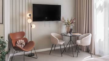 En moderne stue med et fladskærms TV, et rundt bord med to stole, en potteplante og en sofa.