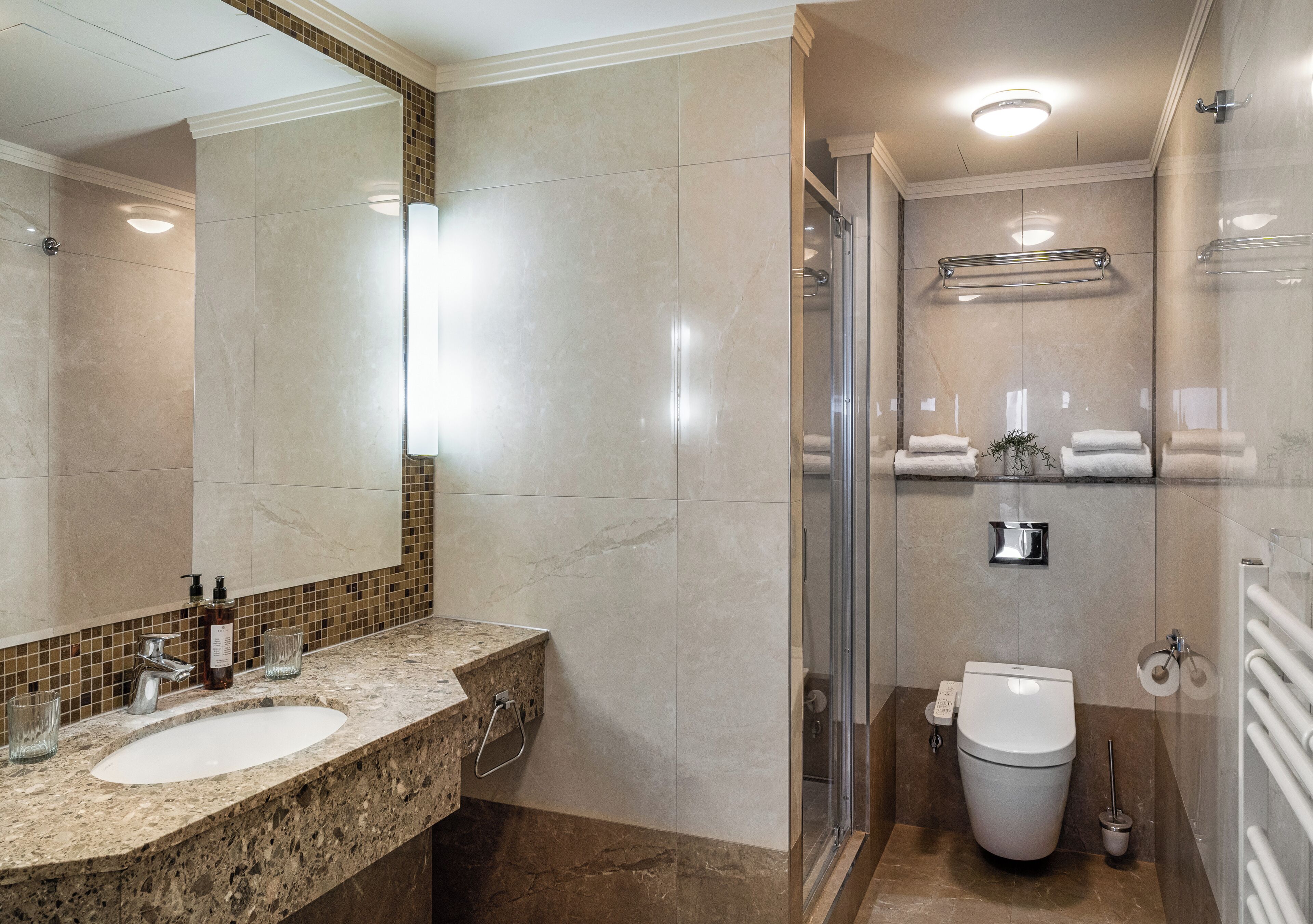 A modern bathroom with a marble sink, a glass shower enclosure, and a toilet with a towel rack.