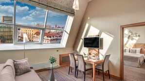 Une chambre d’hôtel dotée d’une grande fenêtre donnant sur la ville, d’un coin salon confortable avec un canapé et une petite table, d’un bureau avec un ordinateur et une chaise, et d’un lit avec une tête de lit en bois.
