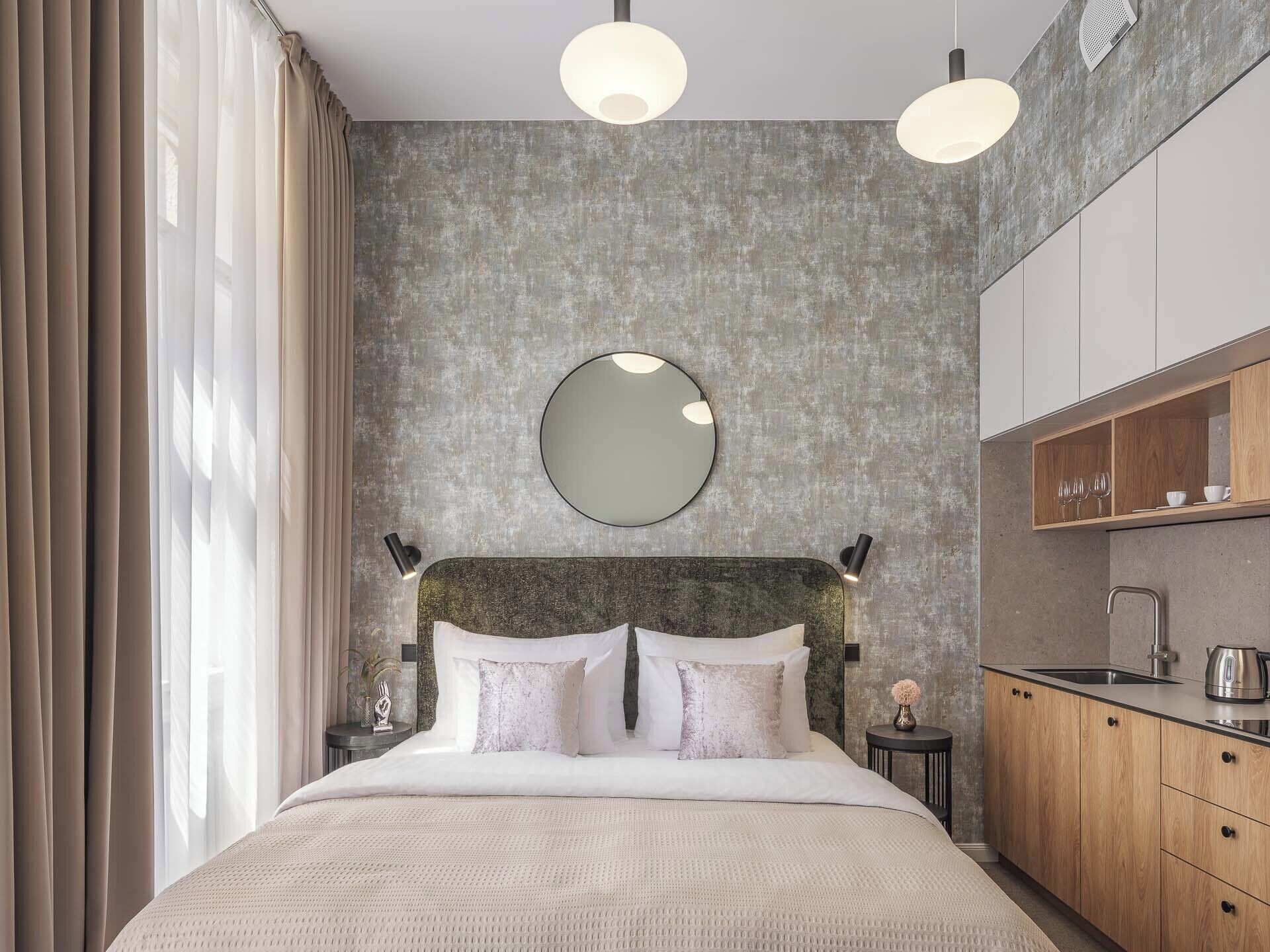 A modern bedroom with a large bed, a round mirror, and a built-in kitchen area.