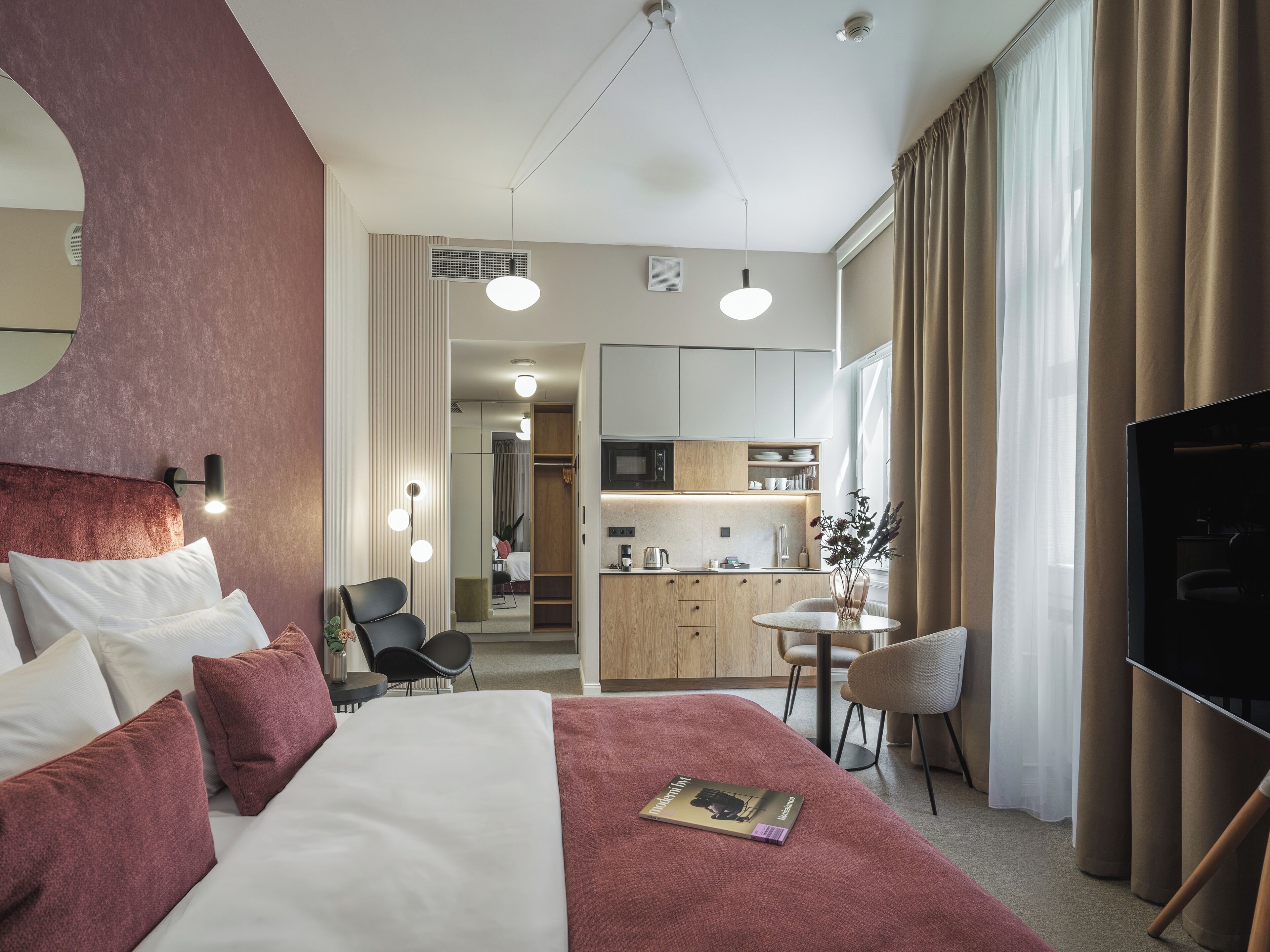 Een hotelkamer met een bed, een bureau, een stoel, een televisie, een kitchenette en een badkamer zichtbaar door een geopende deur.