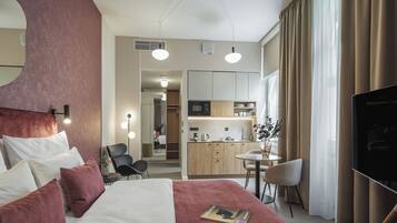 Camera d'albergo con un letto, una scrivania, una sedia, una TV, angolo cottura e bagno visibile attraverso una porta aperta.