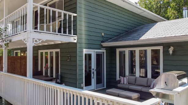 Ein zweistöckiges Haus mit Balkon, überdachter Veranda und Terrasse mit Gartenmöbeln.