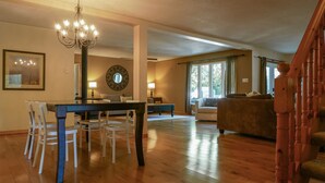Ein geräumiges Wohnzimmer mit Essbereich, einer Chandelierleuchtre, einem großen Spiegel und einer Treppe.