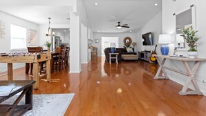 Uma sala de estar ampla com piso de madeira, mesa de pebolim, sofá, mesa de centro e um violão.