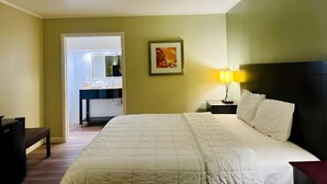 A hotel room with a bed, bedside table, lamp, and a desk with a chair. - Astoria North Extended Stay (Danville)