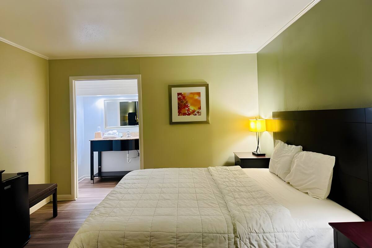 Ein Hotelzimmer mit Bett, Nachttisch, Lampe und Schreibtisch mit Stuhl.
