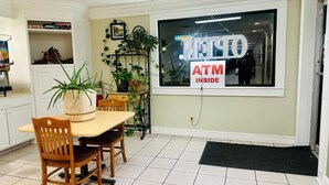 A restaurant with a dining area featuring a table and chairs, a potted plant, and a sign indicating an ATM inside. - Astoria North Extended Stay (Danville)