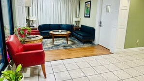 A living room with a red armchair, a blue sofa, a wooden coffee table, and a glass-top table. - Astoria North Extended Stay (Danville)