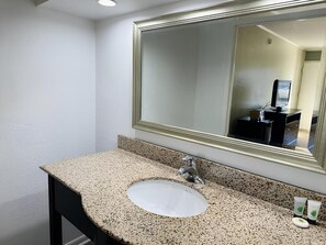 A bathroom with a granite countertop, a sink, a mirror, and a toilet visible in the reflection. - Astoria North Extended Stay (Danville)